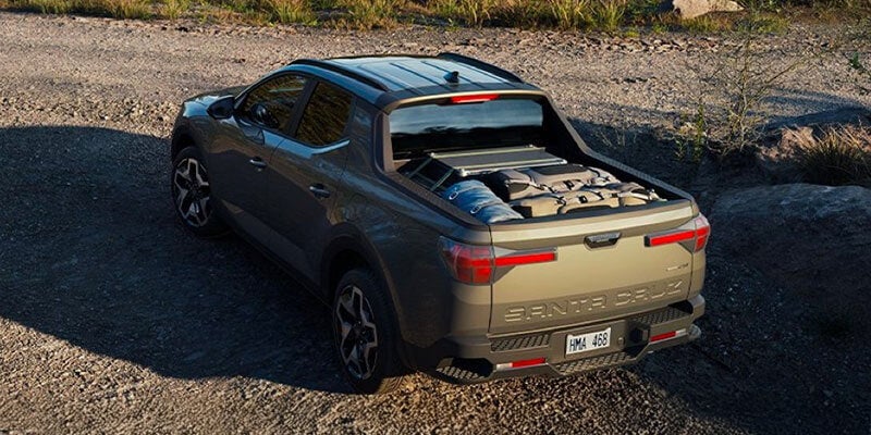 Camioneta Hyundai Santa Fe de color gris oscuro con equipo de campamento en la caja, estacionada en un camino de grava.