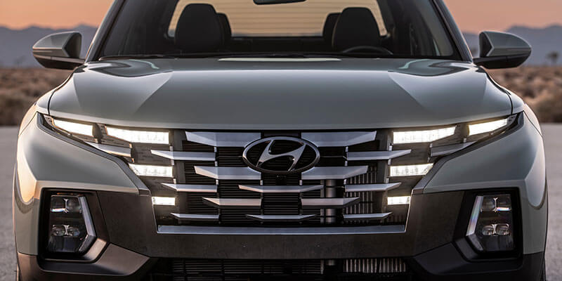 Vista frontal de un automóvil Hyundai gris, que muestra su parrilla cromada con el logotipo integrado y los faros LED iluminados.