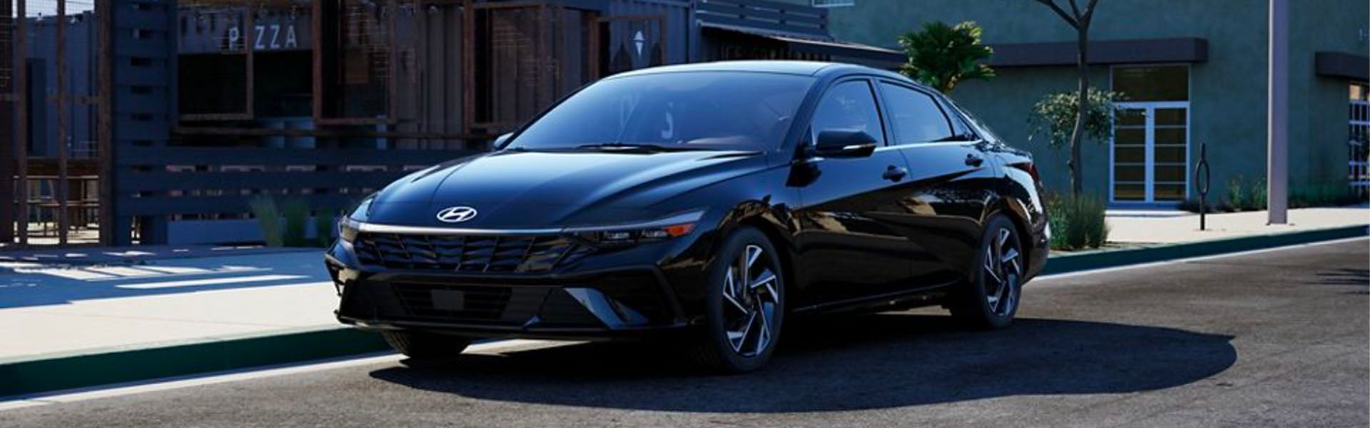 A black Hyundai Elantra parked on an asphalt street with a sidewalk to its left, in front of a modern building.
