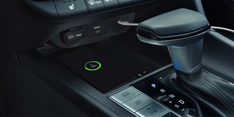 Interior del coche donde se ve un teléfono cargándose de forma inalámbrica sobre una base y un cable USB conectado al salpicadero.