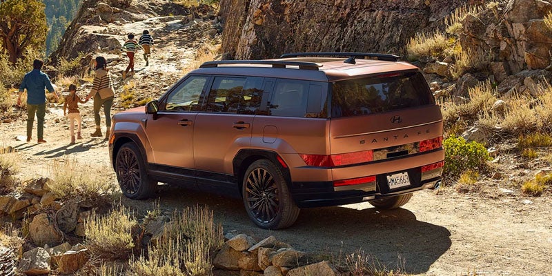 Un SUV Hyundai Santa Fe de color bronce en un sendero rocoso de montaña, con una familia caminando a lo lejos.