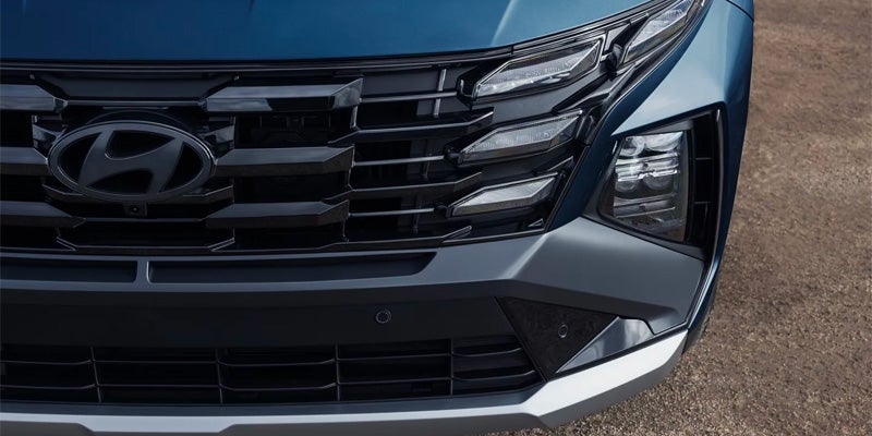 Primer plano de la esquina frontal derecha de un Hyundai Tucson azul oscuro, donde se aprecian la parrilla texturizada y los faros.