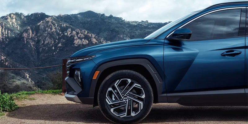 Parte delantera de un Hyundai Tucson azul oscuro estacionado en un camino de tierra, con montañas al fondo.