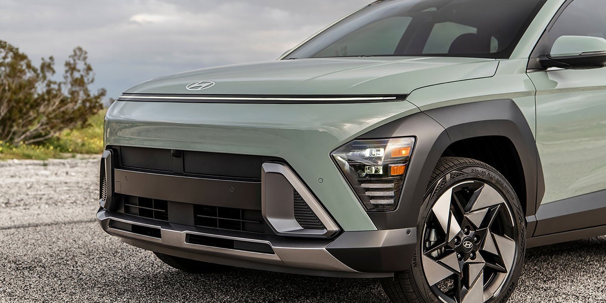 Un Hyundai Kona EV rojo con techo negro circula por una autopista bordeada de vegetación verde.
