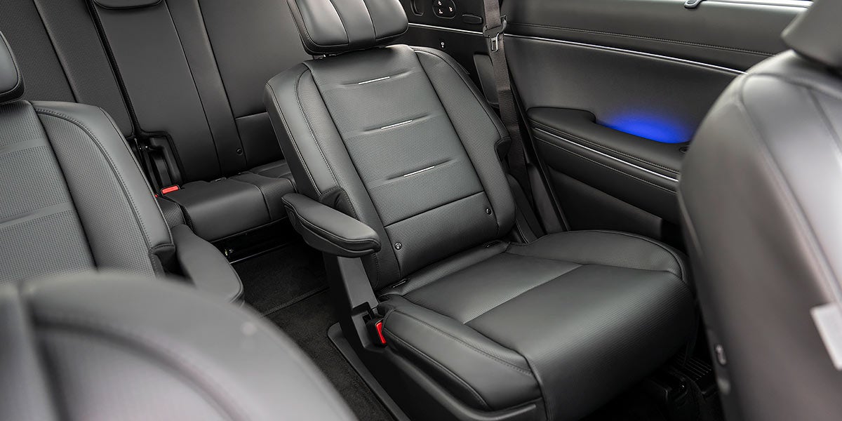 Interior de coche de cuero perforado color beige claro con dos asientos individuales tipo capitán con vistas a un paisaje oceánico y tres personas a bordo.