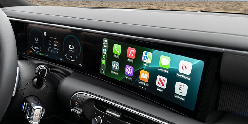 Mano sosteniendo un teléfono inteligente conectado al sistema de infoentretenimiento de un automóvil que muestra Apple CarPlay.