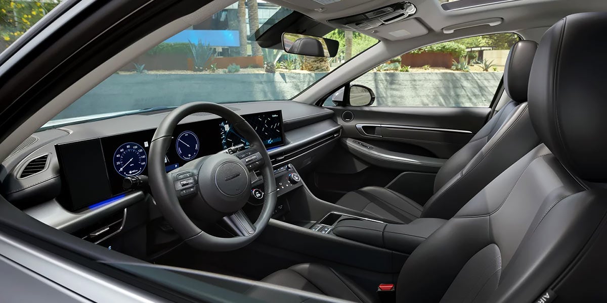 Interior de automóvil moderno con volante multifunción, panel digital y asientos de cuero en diseño elegante.