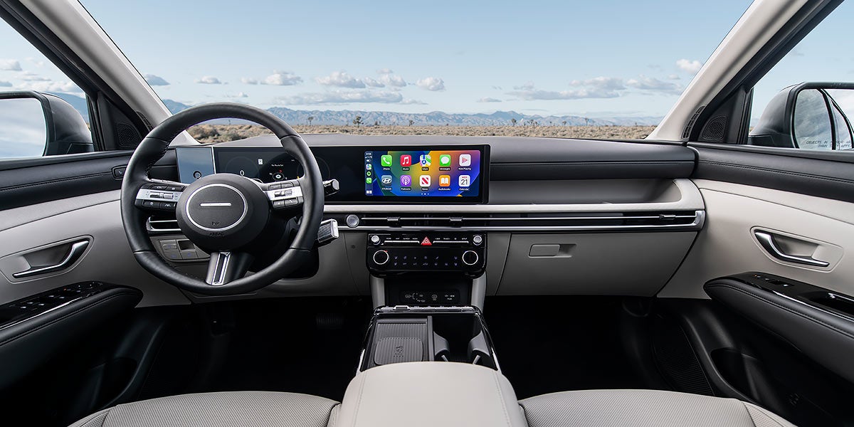 Un conductor sonriente, con gorro y chaleco rojo, se encuentra al volante, con una gran pantalla de infoentretenimiento que muestra las aplicaciones de Apple CarPlay.