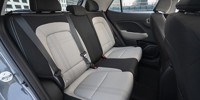 Rear interior view of a car with two dark grey fabric seats featuring subtle plaid patterns and three seat belts.